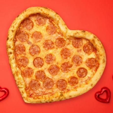herzförmige pizza peperoni zum valentinstag auf rotem papierhintergrund