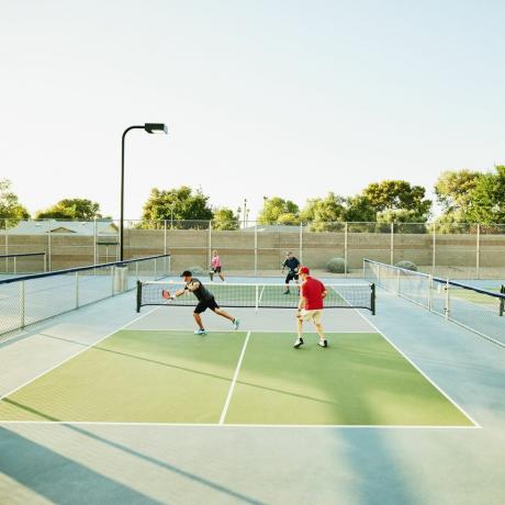 extreme weite aufnahme von älteren freunden, die an einem sonnigen sommerabend doppelt pickleball spielen