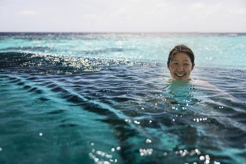 lächelnde Mitte der erwachsenen Frau, die im Infinity-Pool schwimmt