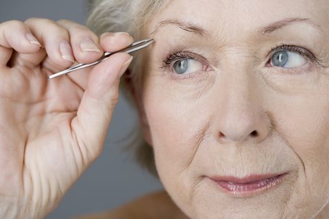 Ältere Frau, die ihre Augenbrauen mit Pinzette zupft