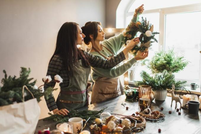 Zwei Frauen basteln einen Weihnachtskranz aus frischen Tannenzweigen und festlichen Dekorationen