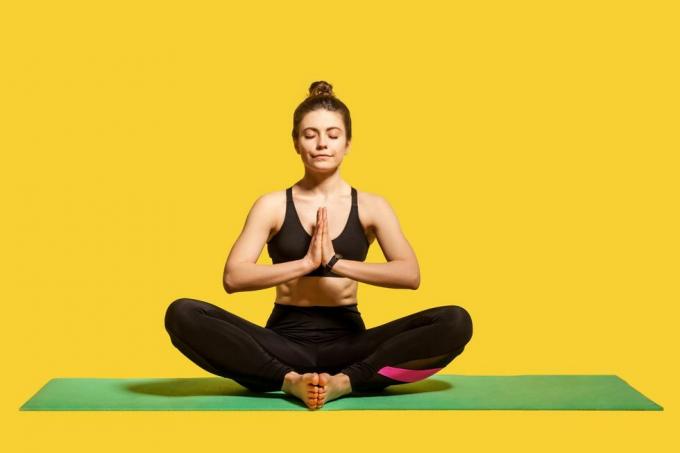 Konzentrierte friedliche Frau mit Haarknoten in enger Sportkleidung, die auf einer Matte sitzt und Yoga praktiziert, Händchen haltend in Namaste