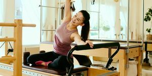 asiatische frau in einem pferdeschwanz und trainingskleidung auf einem pilates reformer