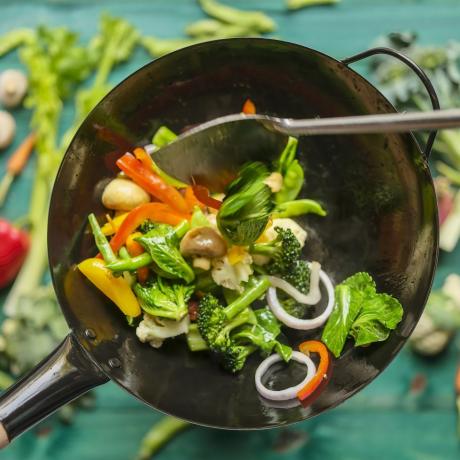Rühren Sie das Braten und Sautieren verschiedener frischer, bunter Marktgemüse in einem heißen, dampfenden Wok mit Gemüse auf einem türkisfarbenen Holztischhintergrund unter dem Wok